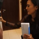 Profissional segura o Vein Viewer Flex, que projeta em luz verde o mapa das veias no braço da paciente.