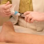 Médica aplica escleroterapia com seringa na perna da paciente, com aplicador de laser ao lado